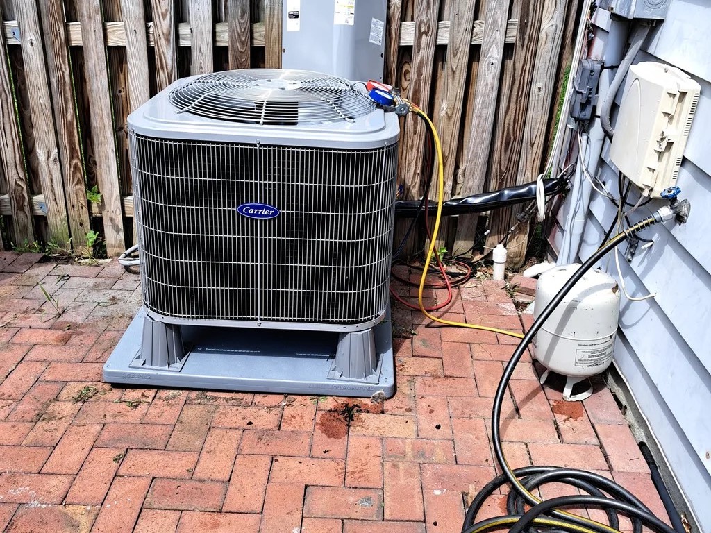 Carrier condenser on a brick patio with a service technician’s hoses connected